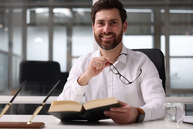 Photo of Smiling man with book at table in office. Lawyer, businessman, accountant or manager