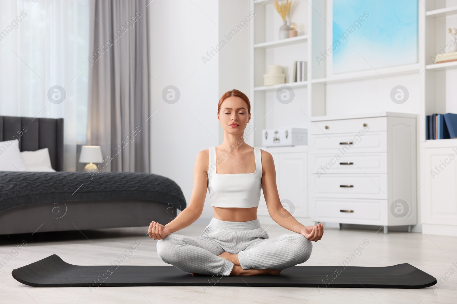 Photo of Beautiful young woman practicing Padmasana on yoga mat at home. Lotus pose