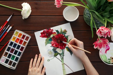 Photo of Woman painting flowers with watercolor at wooden table, top view. Creative artwork