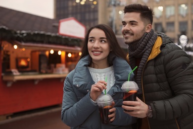 Young couple with cups of mulled wine at winter fair. Space for text