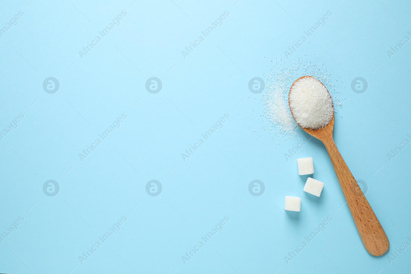 Photo of Sugar and spoon on light blue background, flat lay. Space for text