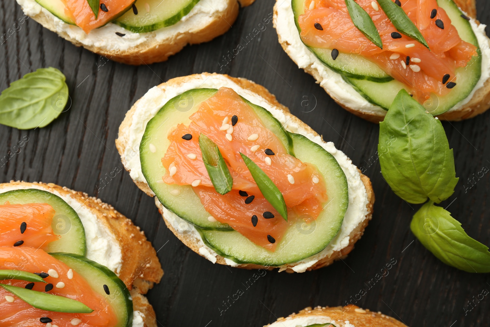 Photo of Tasty canapes with salmon, cucumber and cream cheese on board, top view