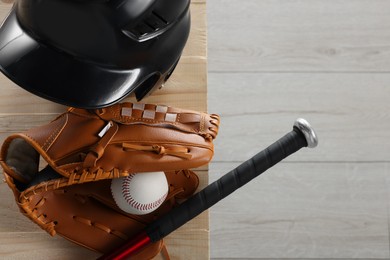 Photo of Baseball bat, batting helmet, leather glove and ball on wooden bench indoors, top view. Space for text