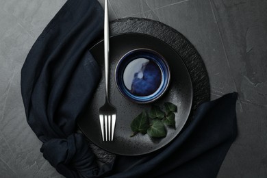 Photo of Stylish table setting. Dishes, fork, napkin and green leaves on grey surface, top view