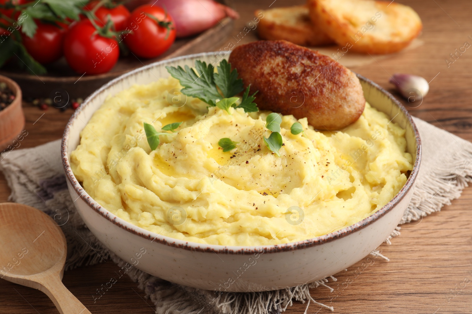 Photo of Bowl of tasty mashed potatoes with parsley, black pepper and cutlet served on wooden table, closeup