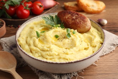 Bowl of tasty mashed potatoes with parsley, black pepper and cutlet served on wooden table, closeup