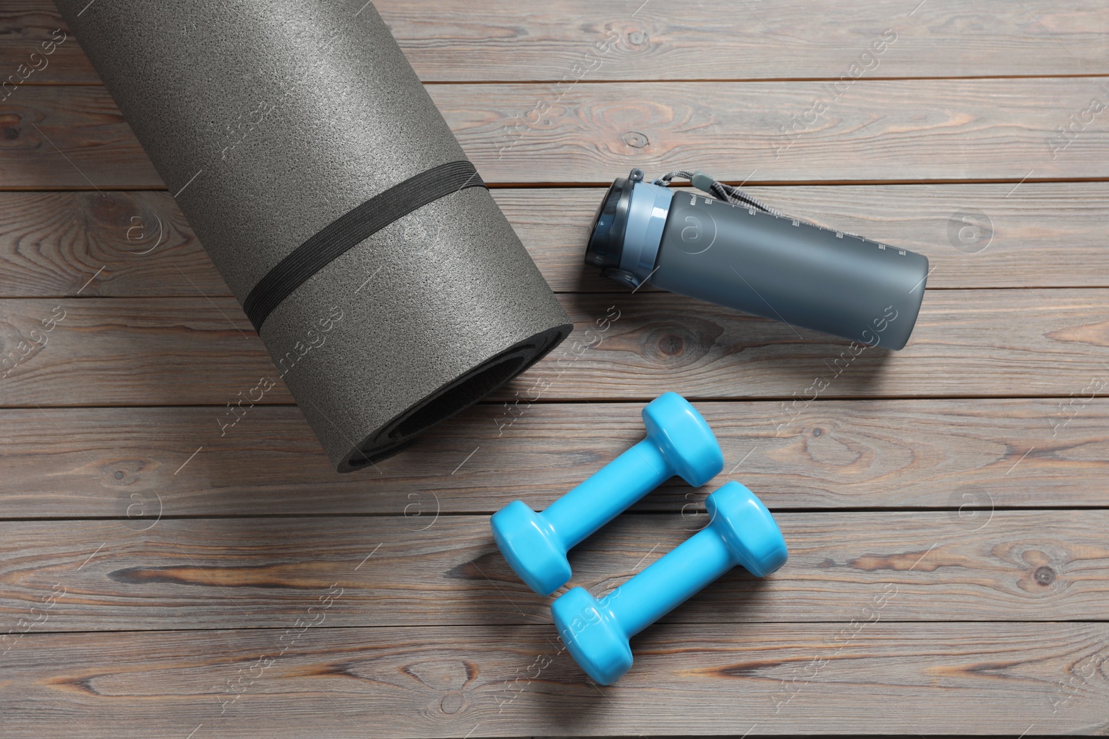 Photo of Yoga mat, bottle of water and dumbbells on wooden floor, flat lay