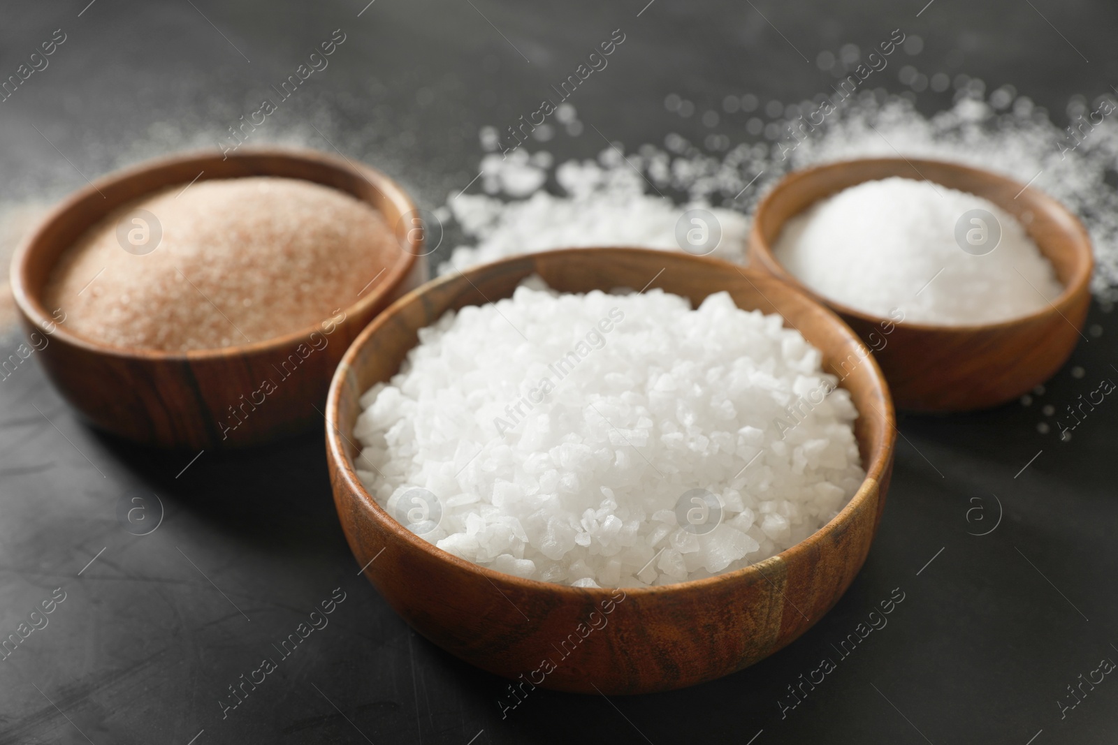 Photo of Different types of organic salt in bowls on black table, closeup