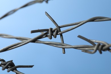 Metal barbed wire on light blue background, closeup