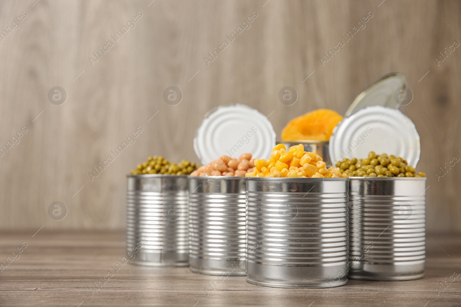 Photo of Open tin cans with conserved vegetables and fruits on wooden table. Space for text