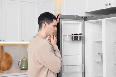 Thoughtful man near empty refrigerator in kitchen