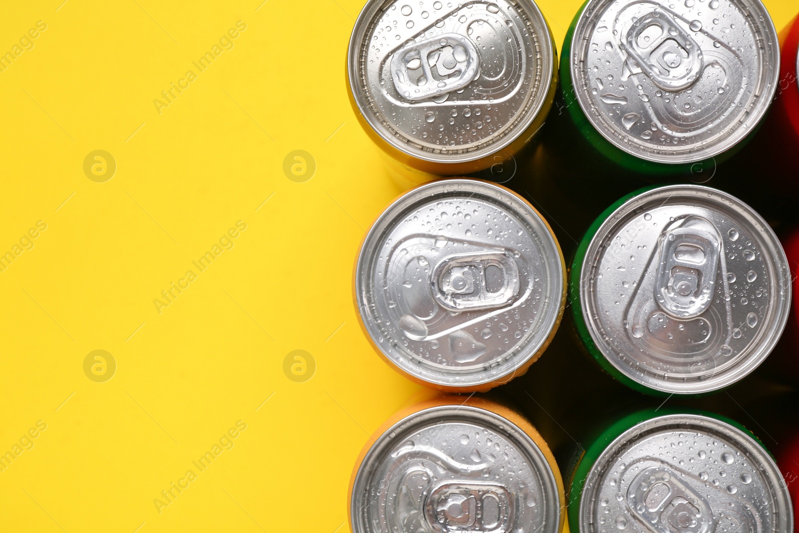 Photo of Energy drinks in wet cans on yellow background, top view. Space for text