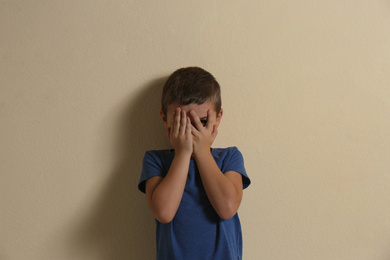 Photo of Scared little boy closing face by hands on yellow background. Child in danger