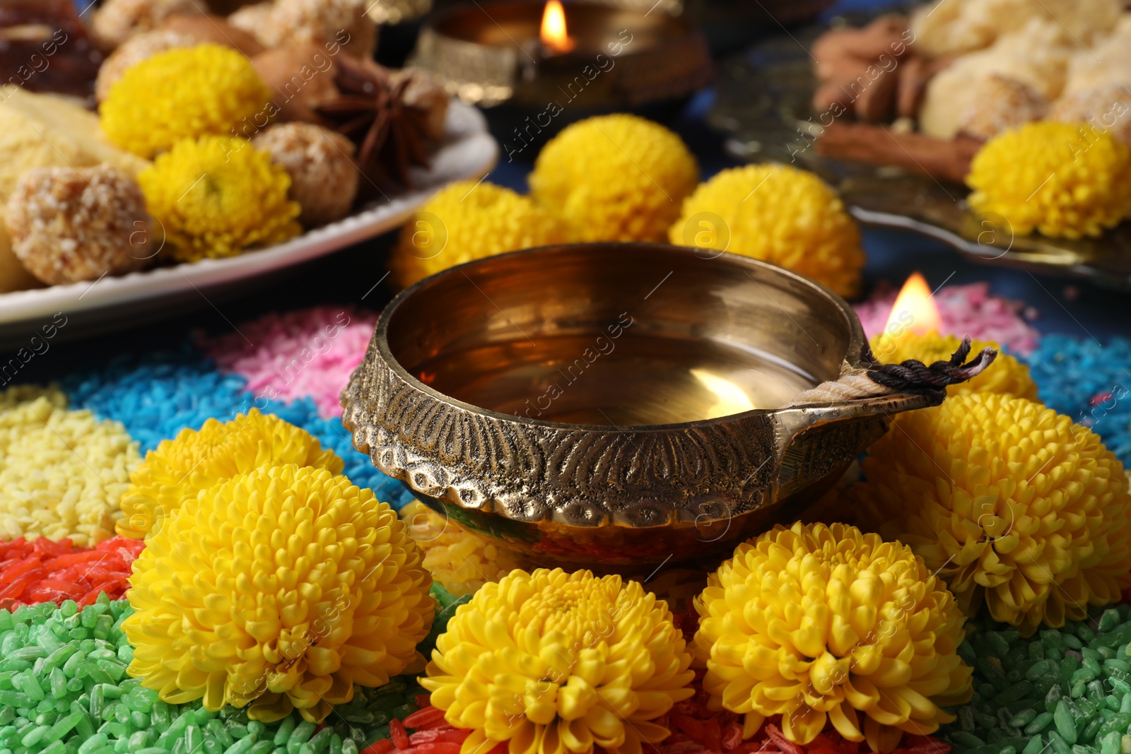 Photo of Diwali celebration. Diya lamp, colorful rangoli and chrysanthemum flowers on table, closeup