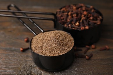 Photo of Aromatic clove powder and dried buds in scoops on wooden table, closeup