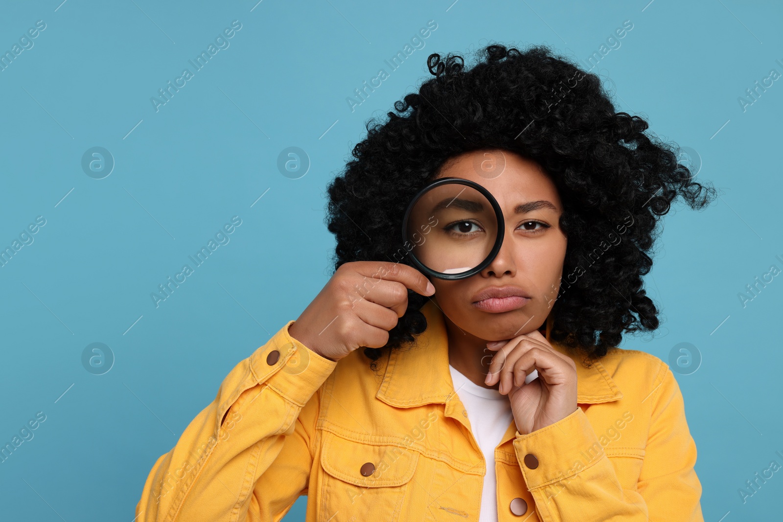 Photo of Woman looking through magnifier glass on light blue background, space for text