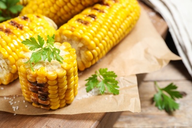 Photo of Delicious grilled corn cobs on wooden table, closeup