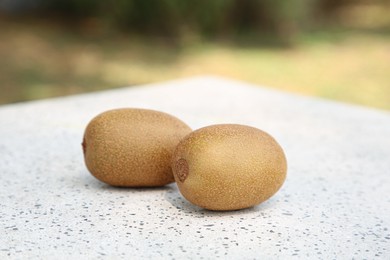 Photo of Whole fresh kiwis on white table with pattern outdoors