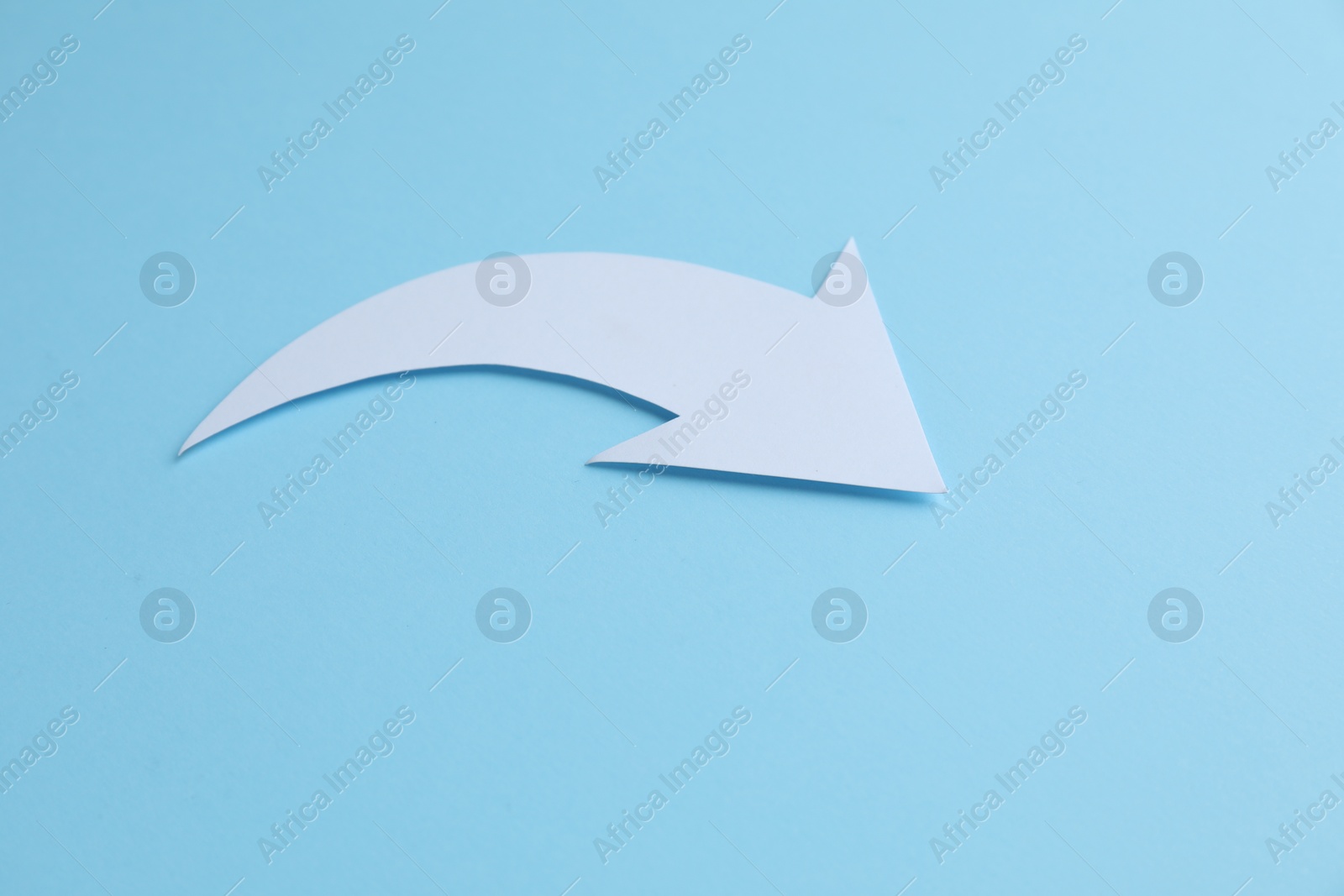 Photo of White curved paper arrow on light blue background, space for text