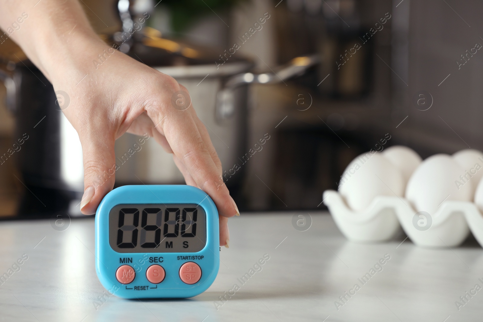 Photo of Woman winding up kitchen timer at white table indoors, closeup. Space for text