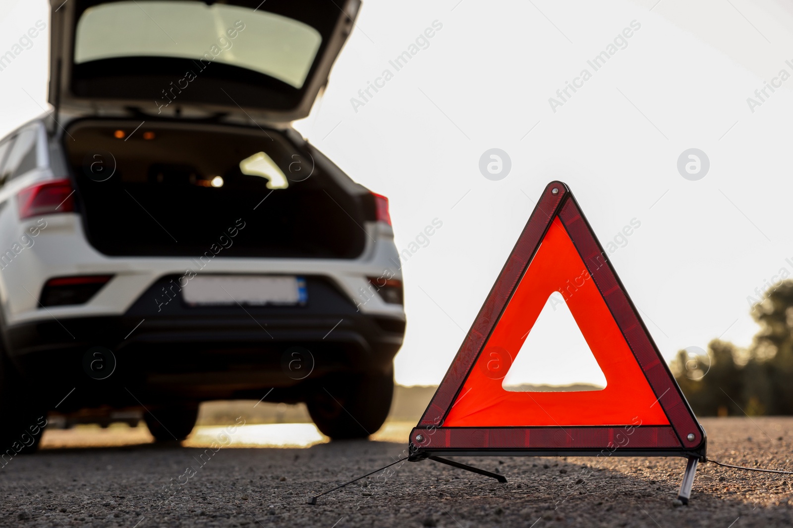 Photo of Warning triangle and broken car on roadside, selective focus