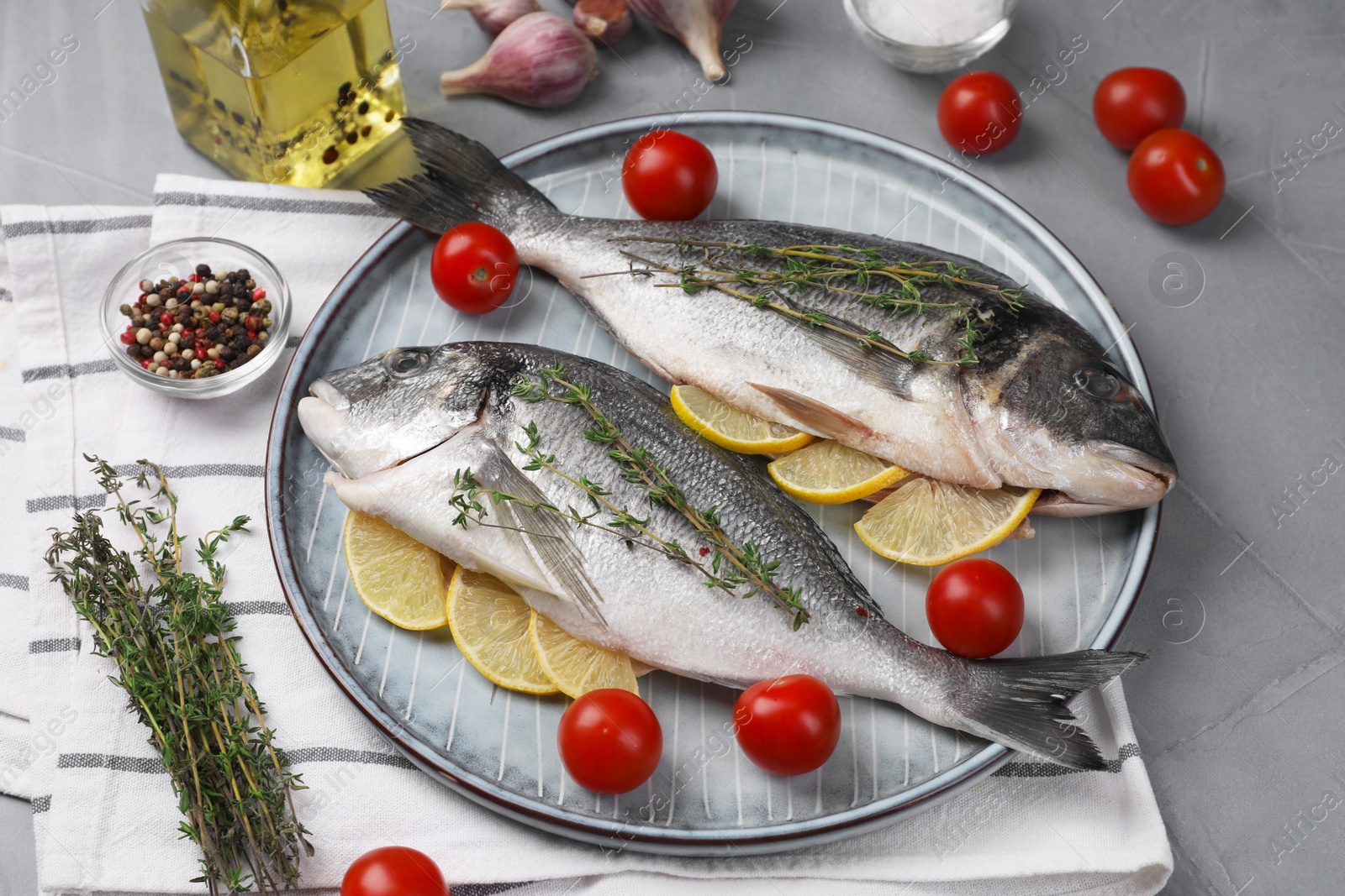 Photo of Raw dorado fish with thyme, lemon slices and tomatoes on grey table