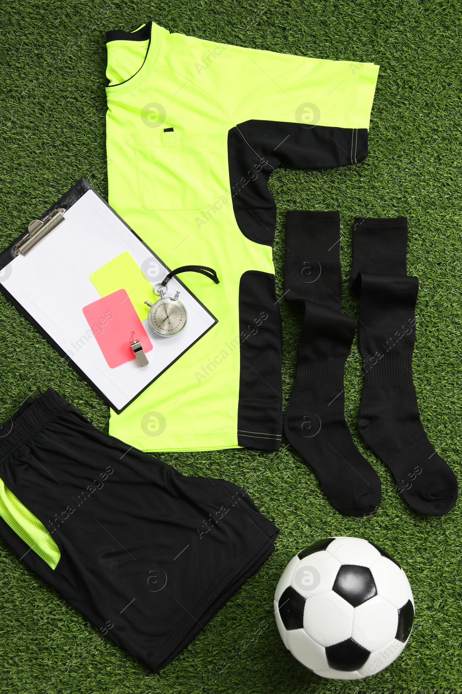 Photo of Uniform, soccer ball and other referee equipment on green grass, flat lay