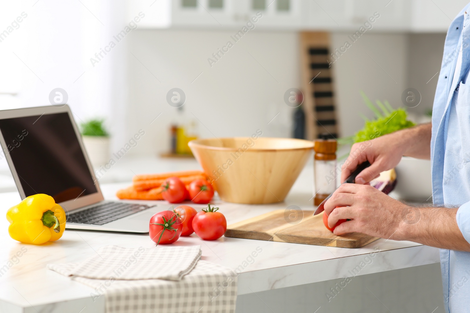 Photo of Man making dinner while watching online cooking course via laptop in kitchen, closeup