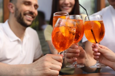 Friends clinking glasses of Aperol spritz cocktails outdoors, closeup