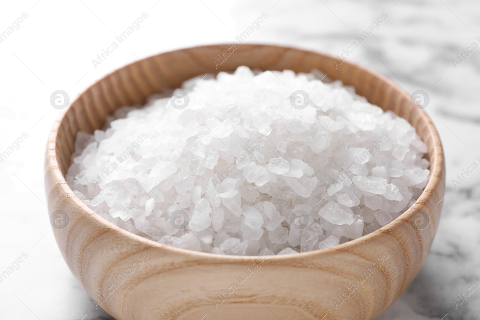 Photo of Wooden bowl with white sea salt on marble table, closeup. Spa treatment