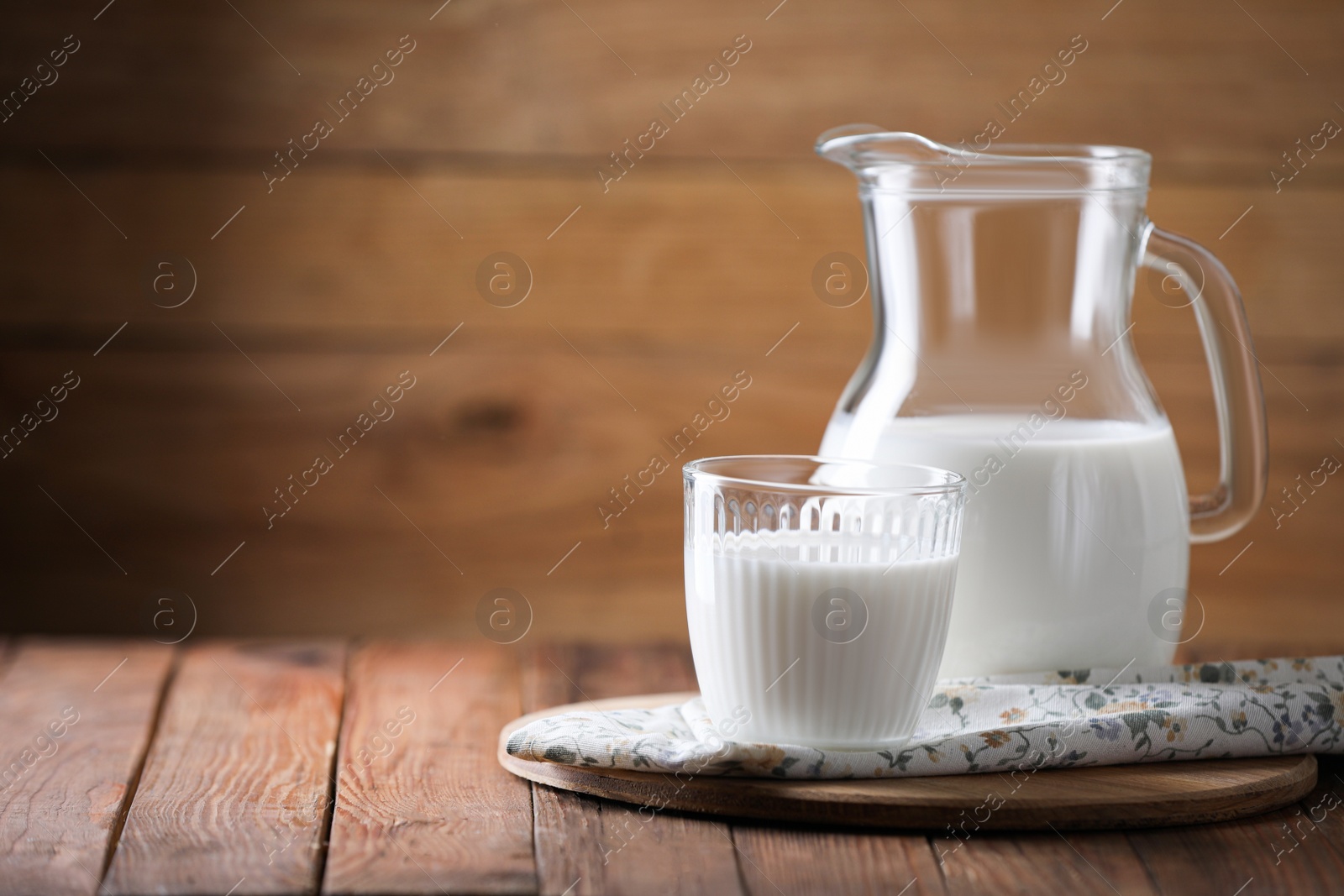Photo of Tasty fresh milk in jug and glass on wooden table, space for text