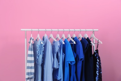 Rack with bright clothes on color background