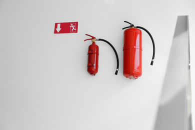 Fire extinguishers and emergency exit sign on white wall indoors