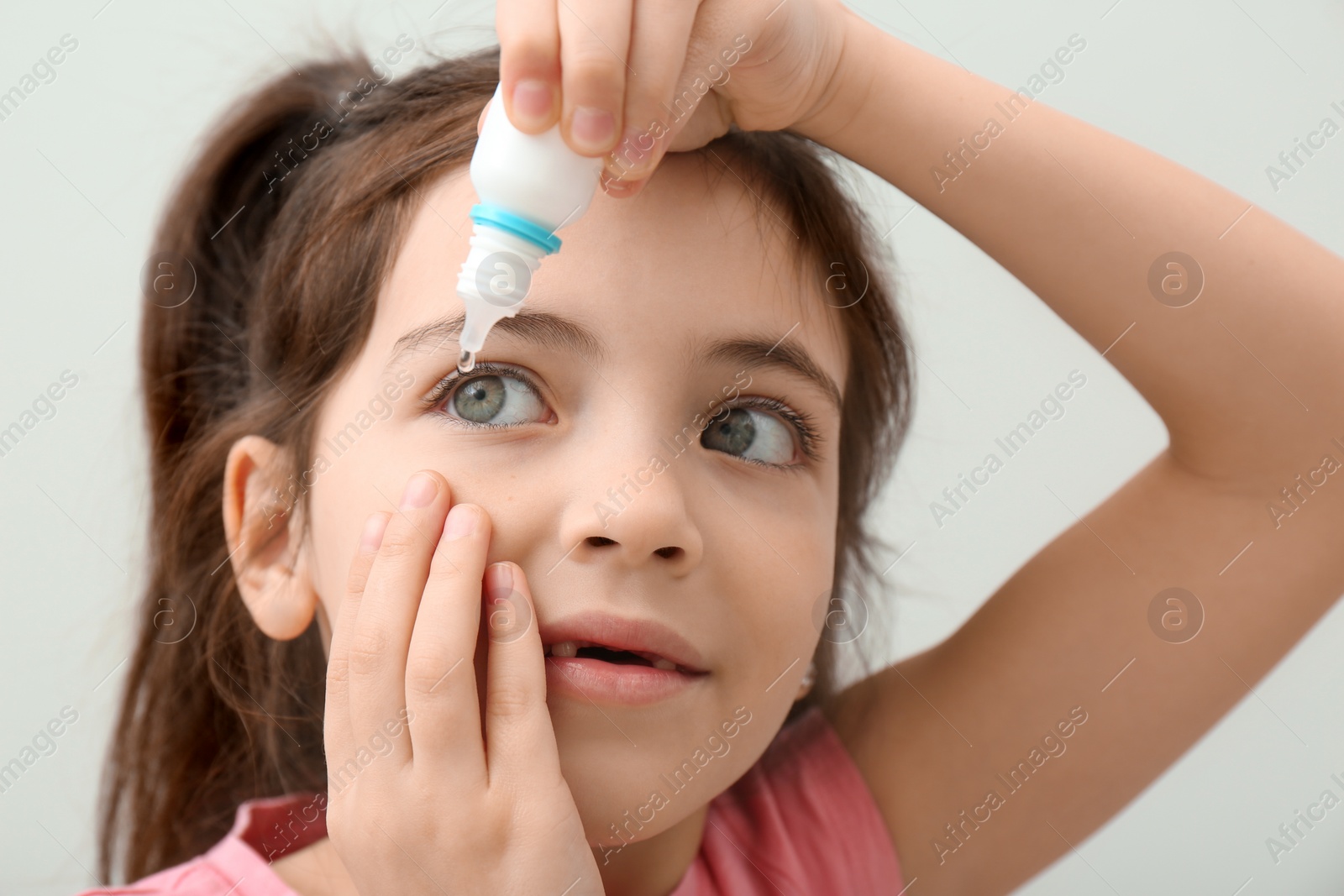 Photo of Adorable little girl using eye drops on white background, closeup