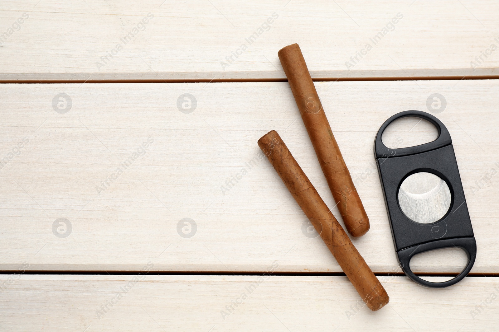 Photo of Cigars and guillotine cutter on white wooden table, flat lay. Space for text