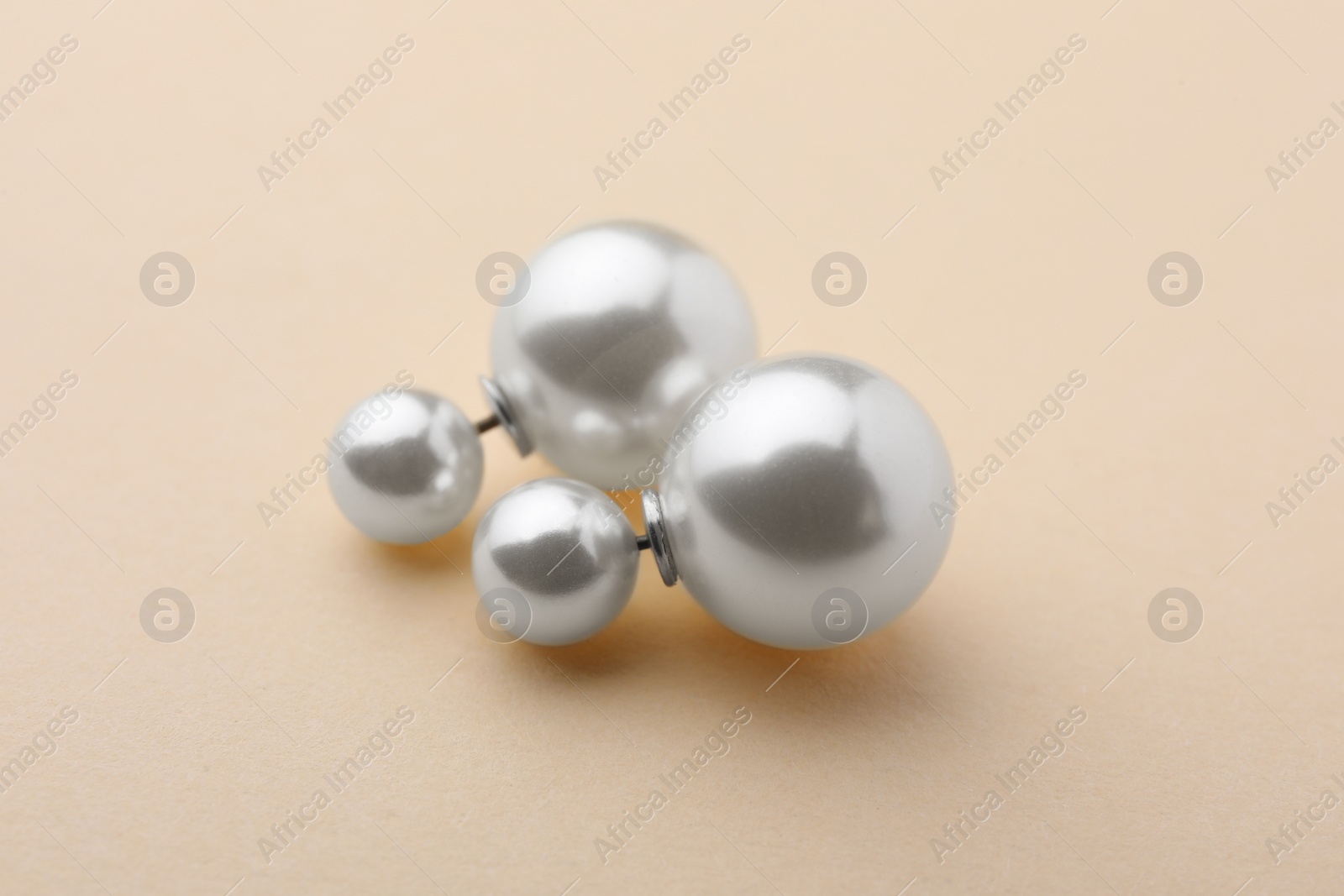 Photo of Elegant earrings with pearls on beige background