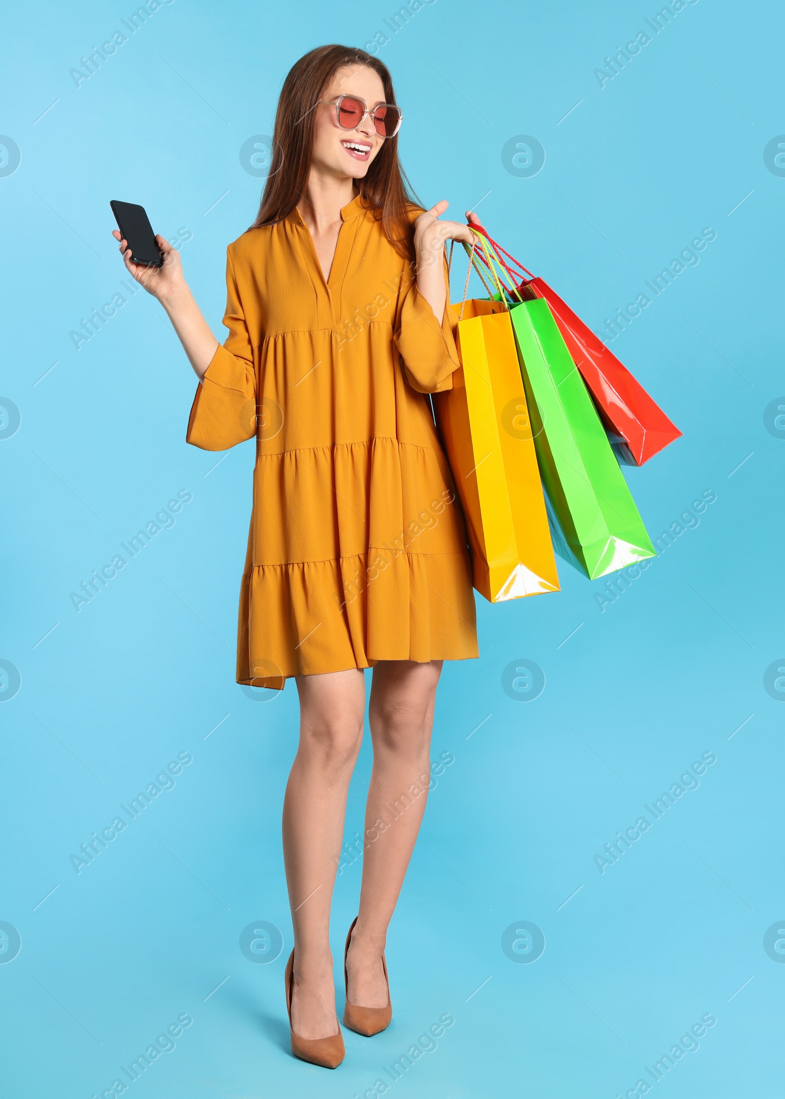 Photo of Happy young woman with shopping bags and smartphone on light blue background. Big sale