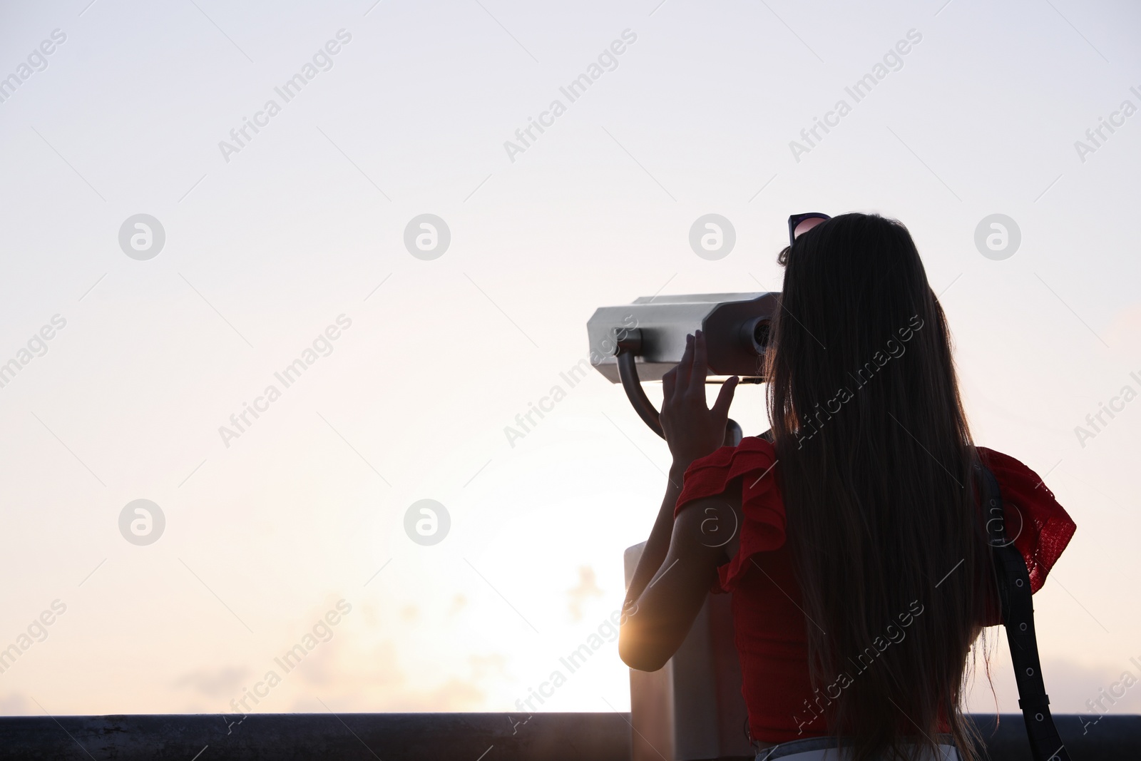 Photo of Young woman looking through tourist viewing machine at observation deck, back view. Space for text