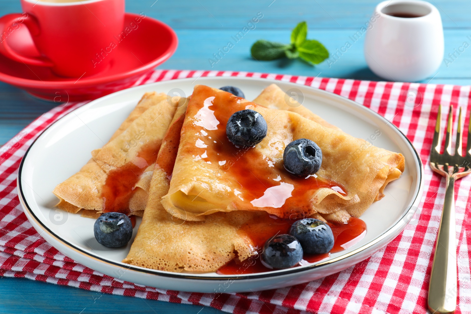 Photo of Delicious crepes served with blueberries and syrup on table, closeup