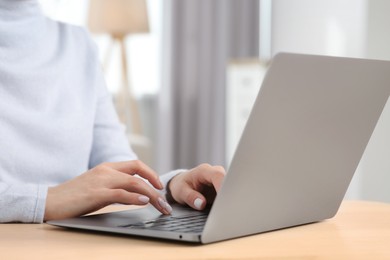 Woman working with laptop at wooden desk indoors, closeup