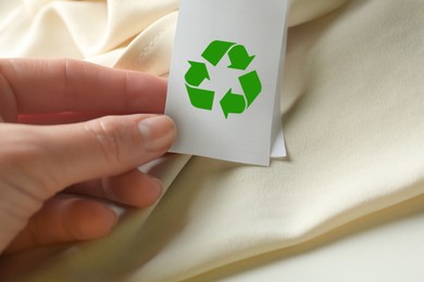 Woman showing clothing label with recycling symbol on beige garment, closeup
