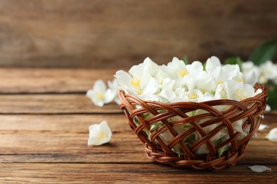 Photo of Beautiful jasmine flowers in wicker bowl on wooden table. Space for text