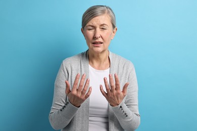 Photo of Arthritis symptoms. Woman suffering from pain in hands on light blue background