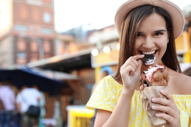 Photo of Pretty young woman eating delicious sweet bubble waffle with ice cream outdoors
