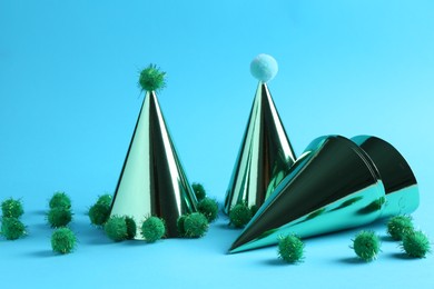 Photo of Party hats with green pompoms on light blue background