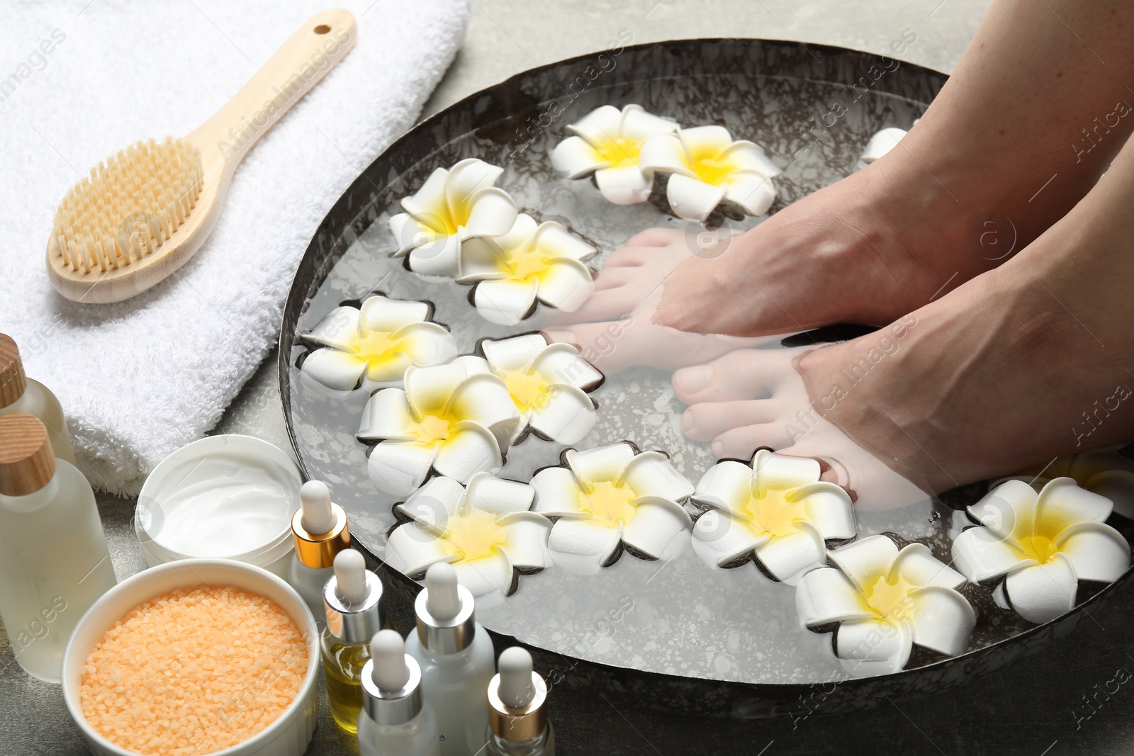 Photo of Woman soaking her feet in bowl with water and flowers on floor, closeup. Spa treatment