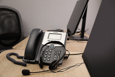 Photo of Stationary phone and headset on wooden desk in office. Hotline service