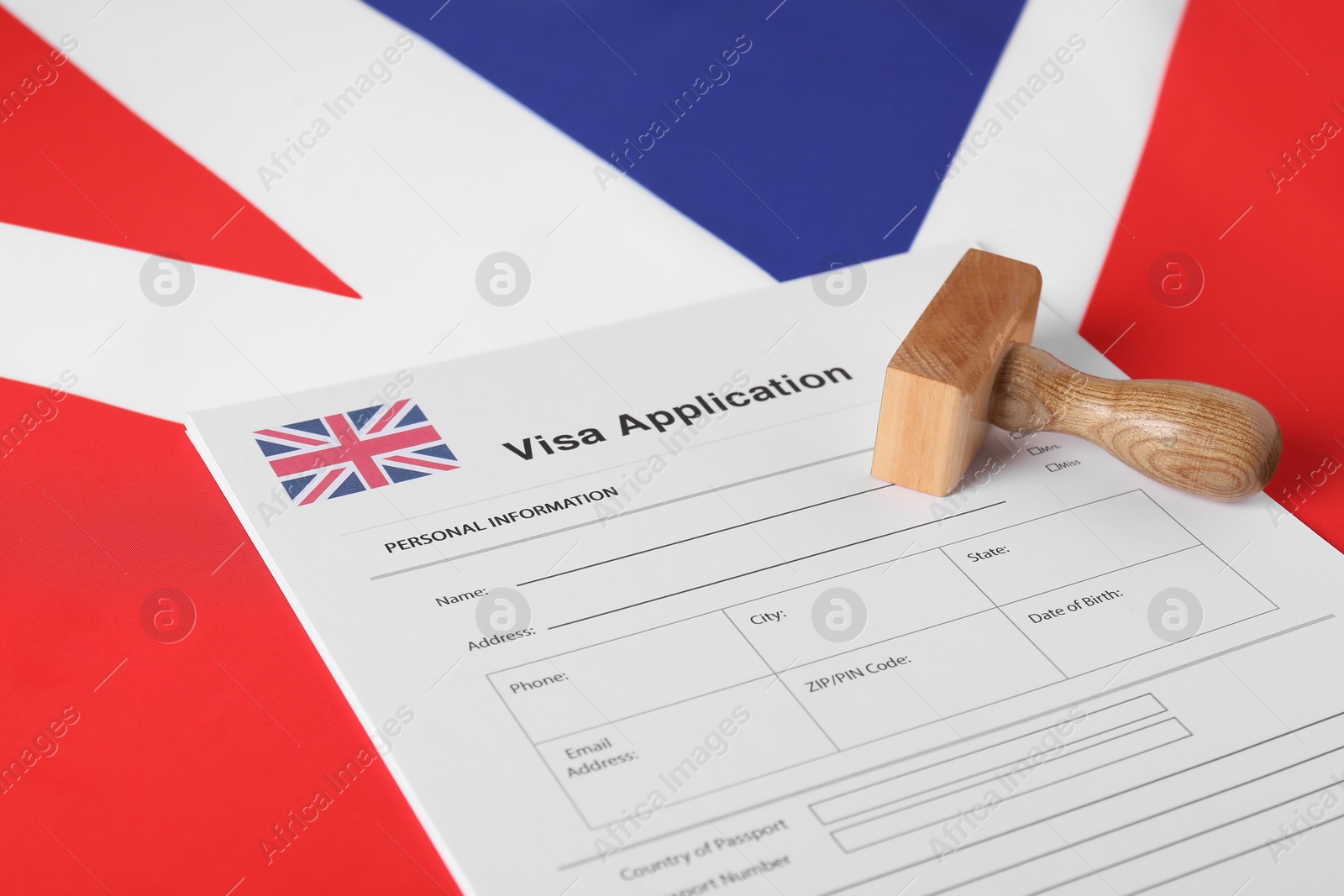 Photo of Immigration to United Kingdom. Visa application form and wooden stamp on flag, closeup