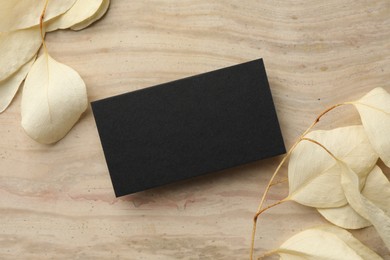 Blank business card and beige leaves on wooden table, flat lay. Mockup for design