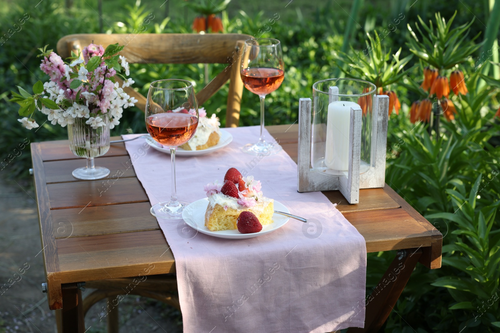 Photo of Vase with spring flowers, wine and cake on table served for romantic date in garden